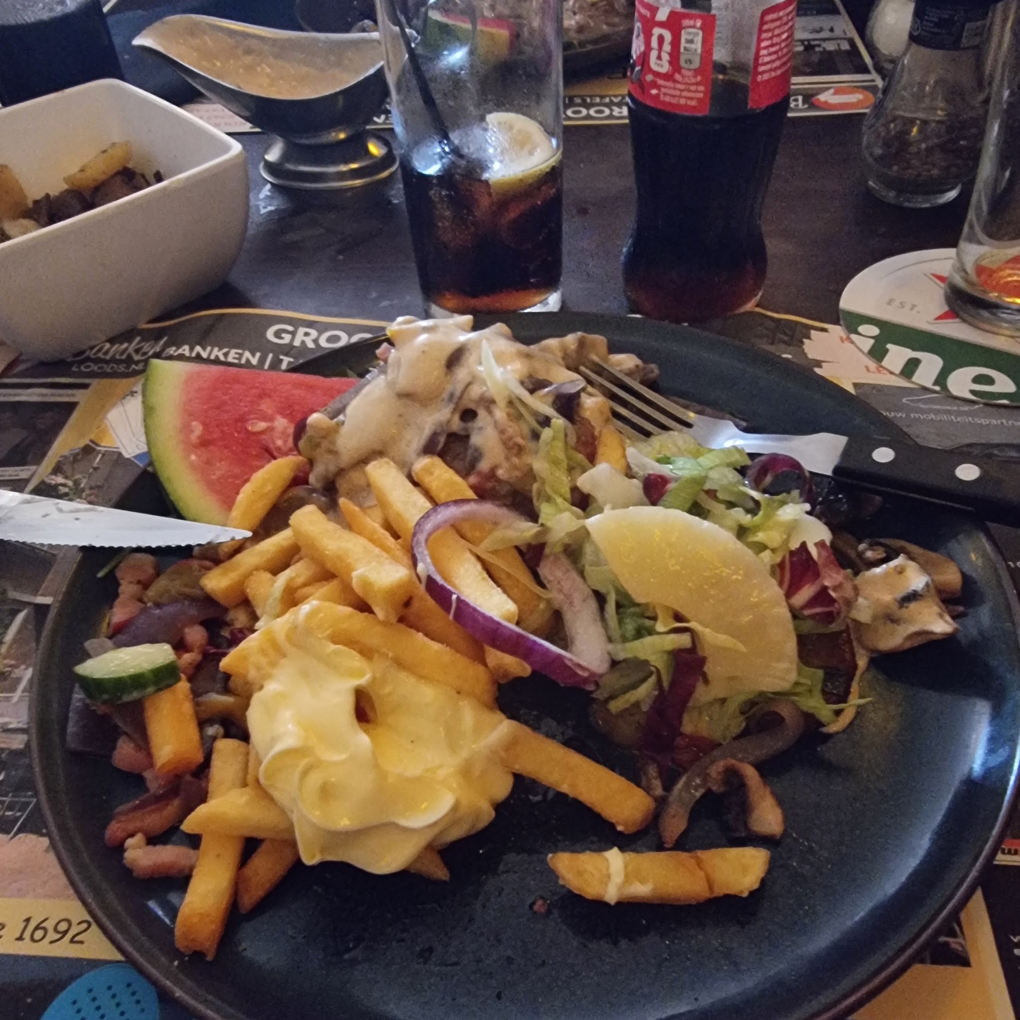 Een ruime schaal met friet, vlees, salade en saus op tafel bij Full House