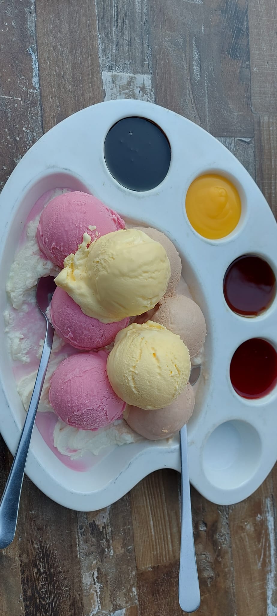 Een paletvormig bord met gekleurde bolletjes ijs en verschillende sauzen