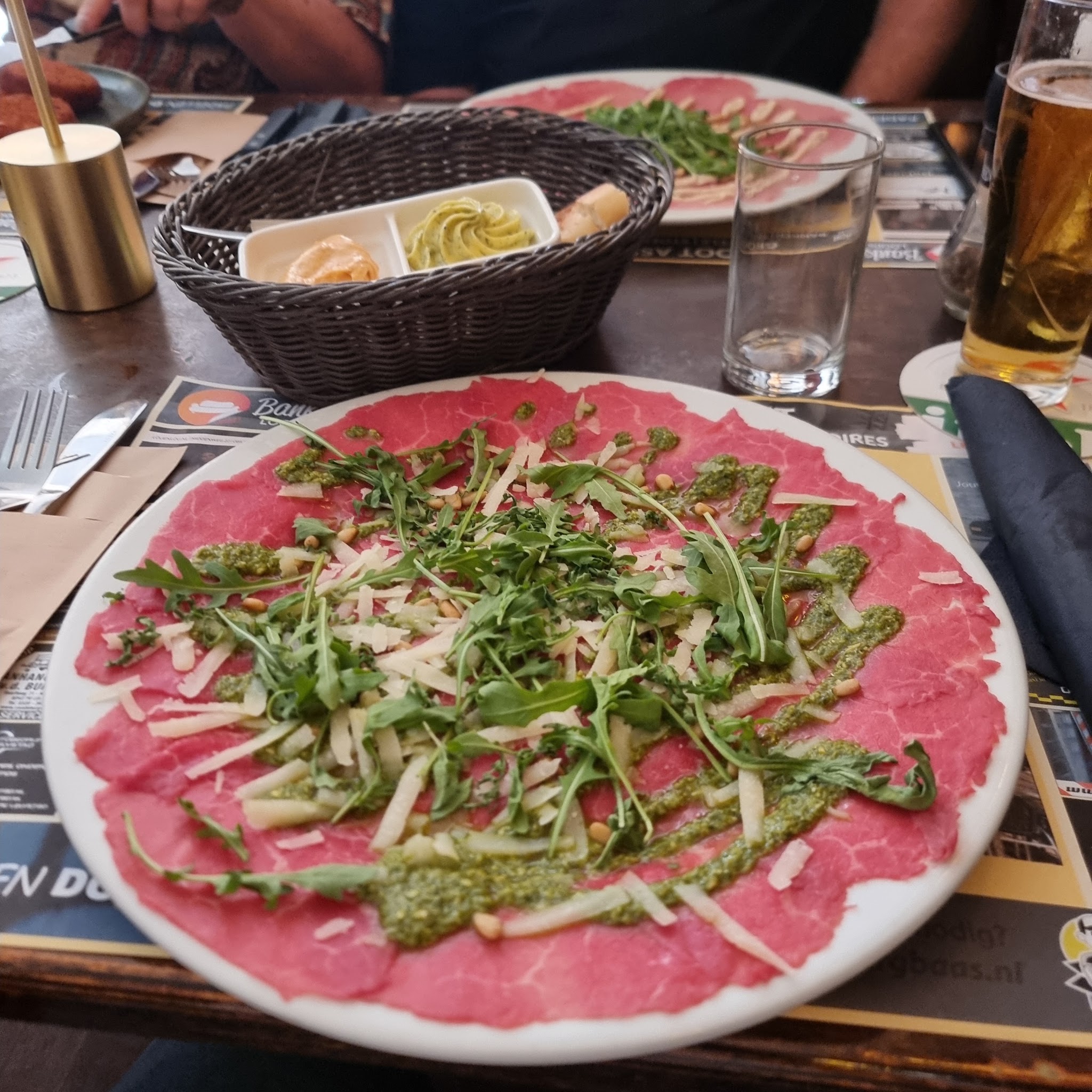 Een bord carpaccio met rucola, kaas en pijnboompitten